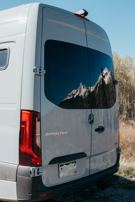 White Mercedes-Benz Sprinter van RV rental reflecting majestic mountains, ideal for scenic adventures.