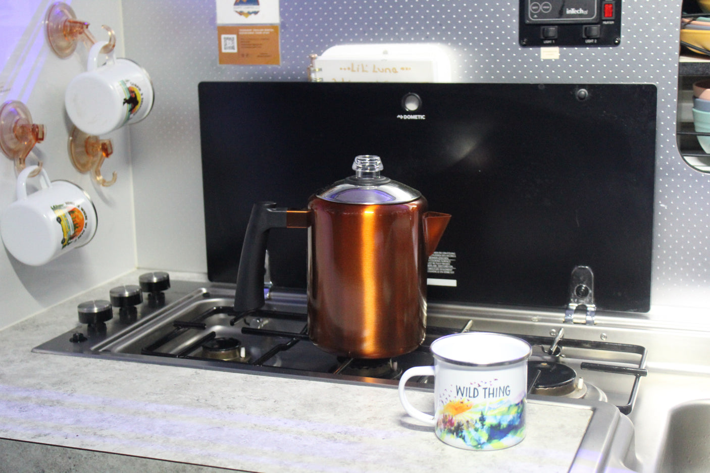 Inside an RV rental: a compact kitchen featuring a stove with a copper percolator and a "WILD THING" mug.