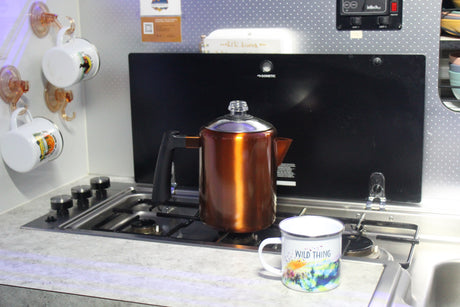 Inside an RV rental: a compact kitchen featuring a stove with a copper percolator and a "WILD THING" mug.