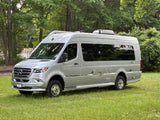 A sleek silver Mercedes-Benz Sprinter RV rental, appearing to be an Airstream Interstate, parked on lush green grass.
