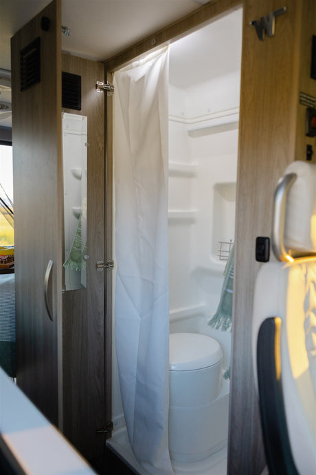 Compact RV rental bathroom with shower, toilet, and mirror, showing efficient interior design for travel.