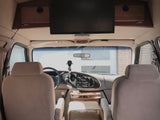 Interior of an RV rental, showing the front cabin with two tan seats, dashboard, and an overhead TV.