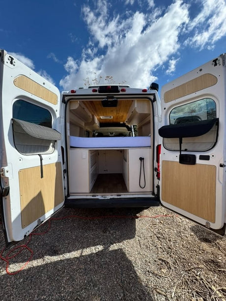 Back of an RV rental camper van with open doors, revealing a bed & storage. Ready for your mobile living adventure.