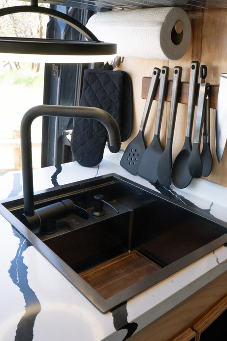 Modern black sink & faucet in a stylish rv rental kitchen, with hanging utensils & paper towel holder. Ready for travel!