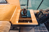 Modern RV rental interior: sleek induction cooktop with kettle, wooden countertop, cozy bed, and fridge.
