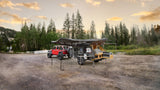 RV rental: Red Jeep with an overland camper, awning, & outdoor kitchen set up for wilderness camping in a mountain clearing.