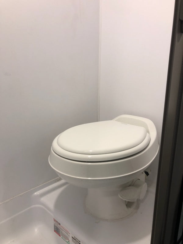 A white toilet with a foot pedal in an RV rental bathroom. Shows typical compact RV facilities.