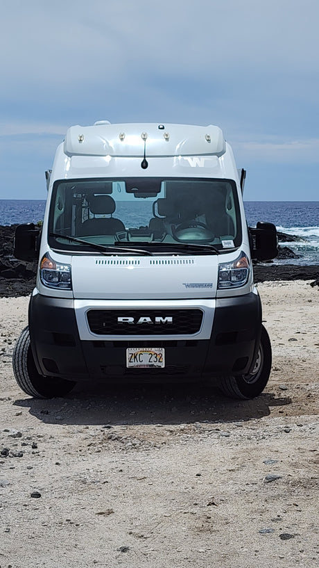 White Ram Promaster RV rental on a gravel path near the ocean.