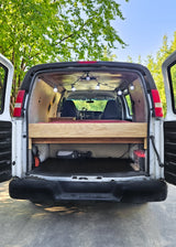 Inside an RV rental, a converted camper van features a wooden bed frame, string lights, and under-bed storage for gear.