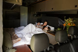A family (mother and two children) cozy in bed inside a modern rv rental, starting their day. Features a compact living space.