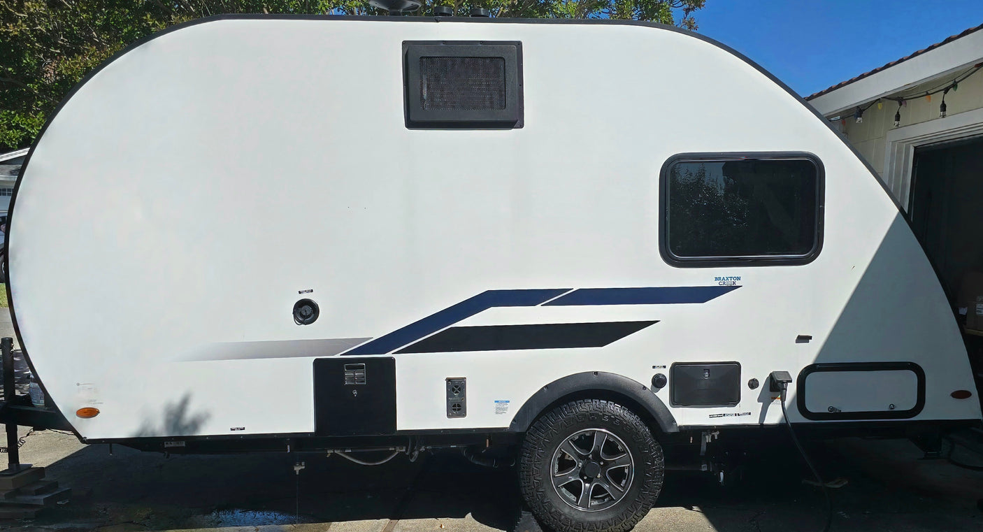 White compact RV rental travel trailer with black accents and rugged tires, ready for camping adventures.