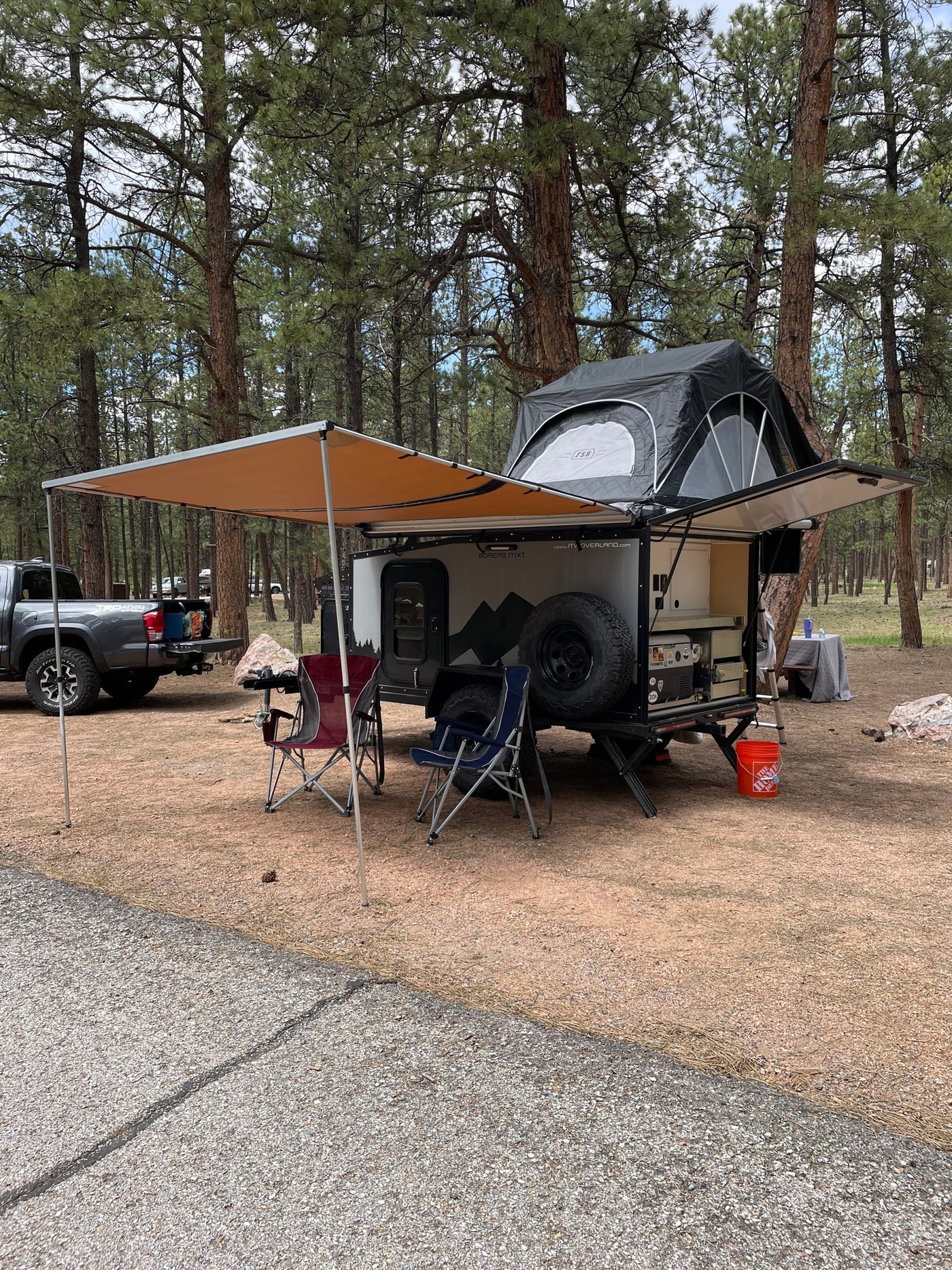 This RV rental overland trailer, featuring a rooftop tent and awning, is set up for camping in a peaceful pine forest. — photo 10
