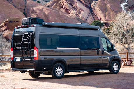 Dark grey Tellaro RV rental camper van with a bike rack, parked amidst scenic red rock formations.