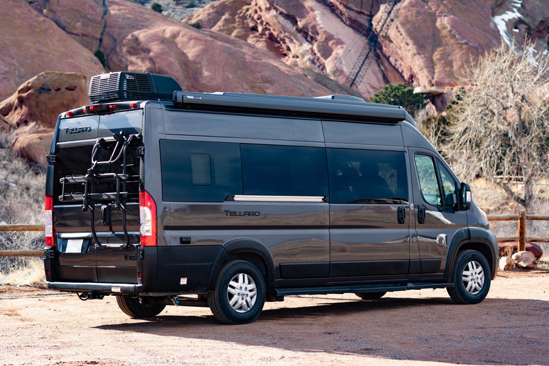  ideal for exploring rocky landscapes.|A dark gray camper van sits on a dirt road with red rock formations in the background. Ideal for an RV rental adventure.|Dark grey Tellaro RV rental camper van with a bike rack — photo 8
