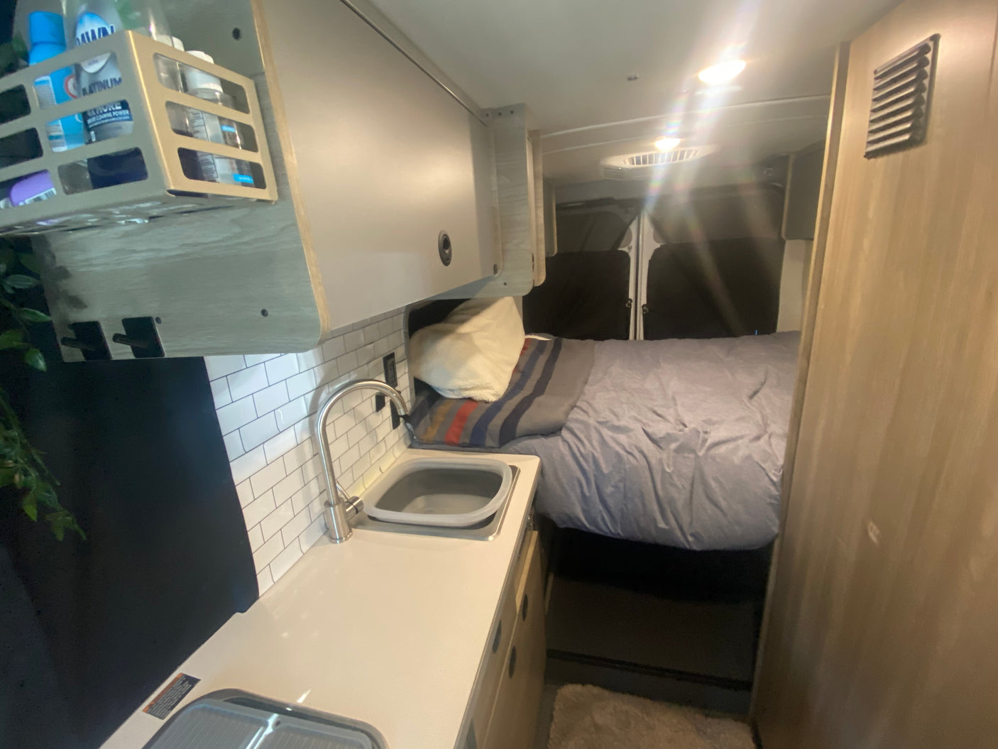 Inside this RV rental: a cozy bed, compact kitchenette with sink, and overhead storage. Ideal for road trips.