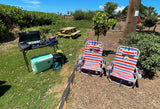 Sunny outdoor setup for your RV rental: portable kitchen, cooler, picnic table, and comfy striped lounge chairs.