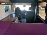 Wayfarer Vans RV rental interior: purple bed, kitchen, and cockpit view. Mobile living ready for your next road trip.