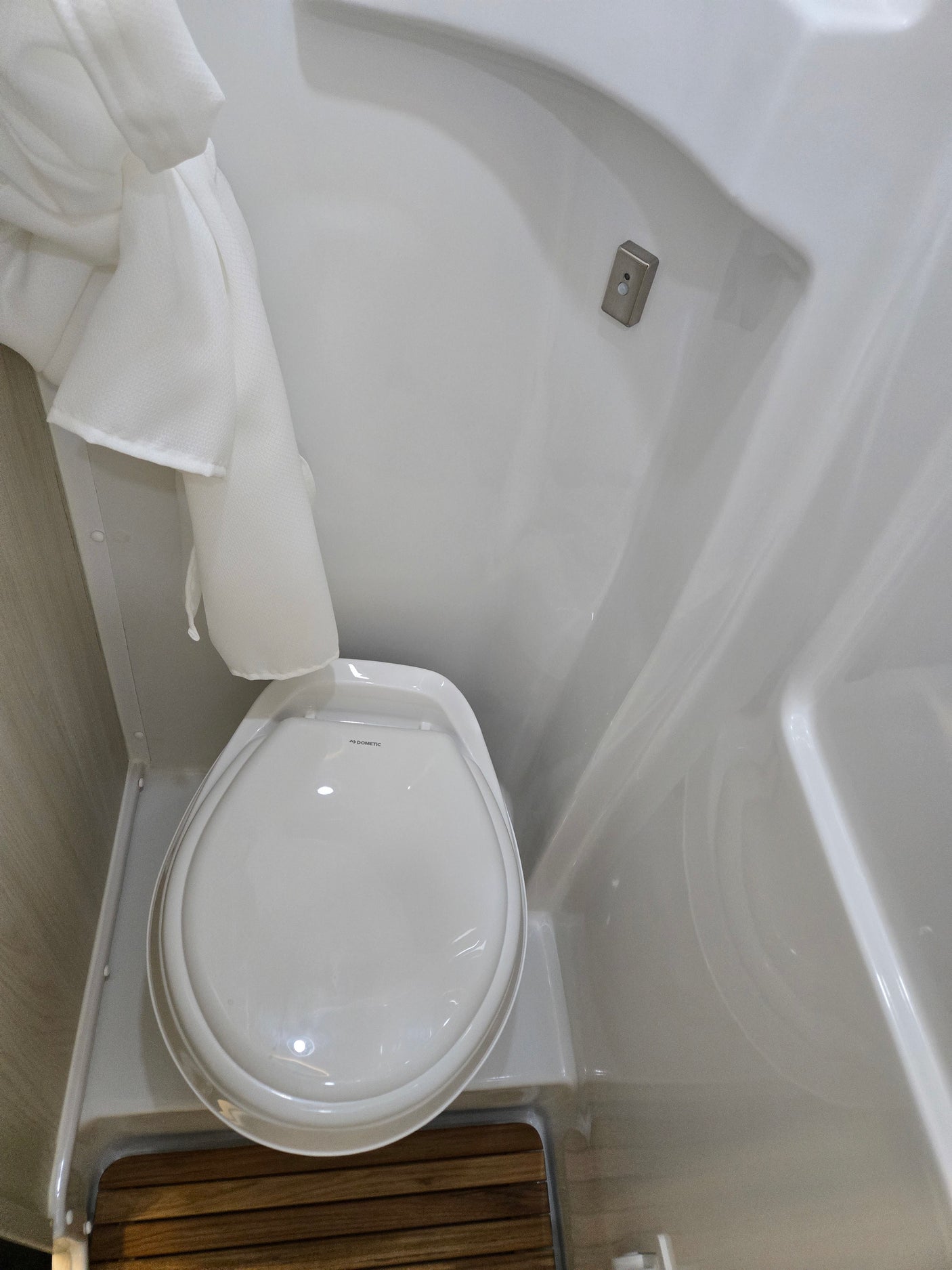 Inside an rv rental, a compact Dometic toilet is shown in a small, white wet bath with a shower curtain and slatted wood floor.