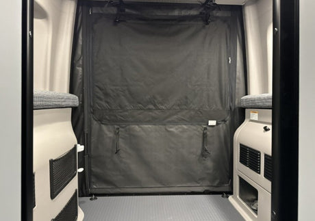 RV rental interior looking to the rear. Black privacy curtain, side benches with storage, and grey floor.