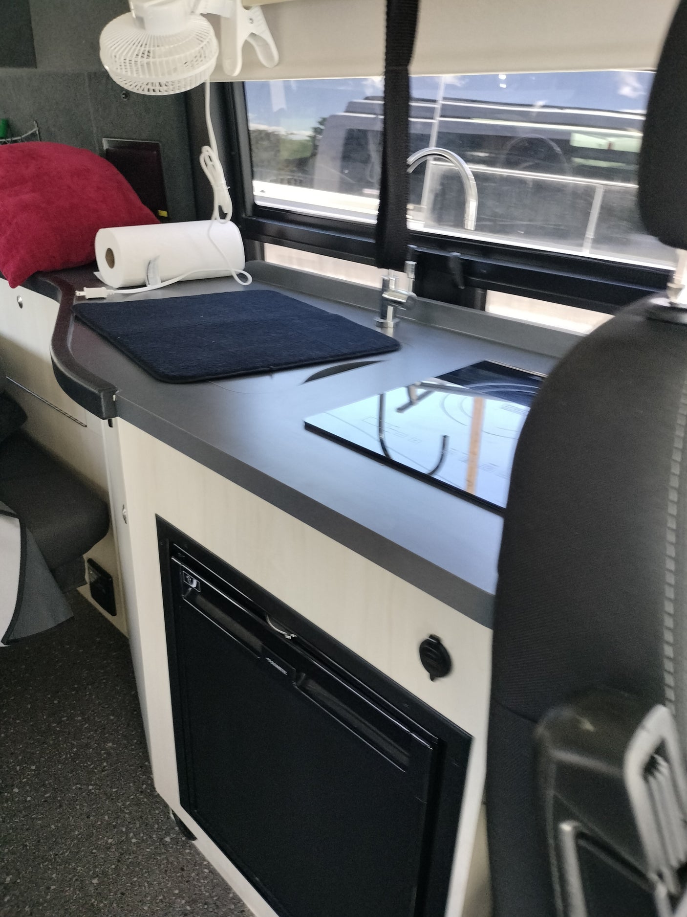 RV rental interior: modern kitchenette with sink, induction cooktop, under-counter fridge, plus fan and window view.