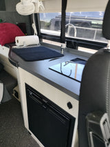 RV rental interior: modern kitchenette with sink, induction cooktop, under-counter fridge, plus fan and window view.