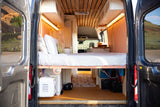 Rear doors open to a custom rv rental camper's cozy interior with a bed, wood ceiling, and off-grid utilities.