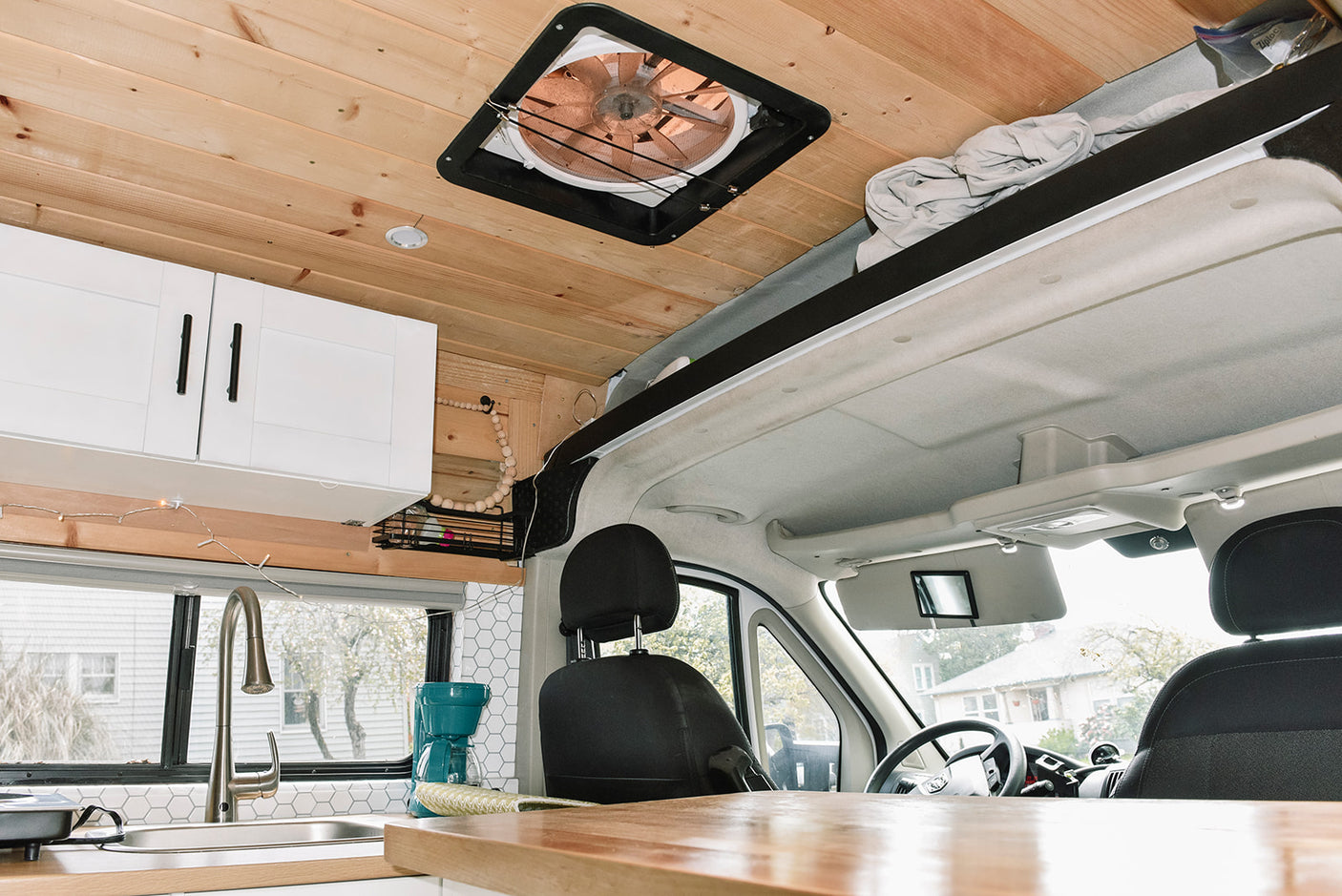 View from inside an RV rental showing the kitchen area with white cabinets, sink, and wood ceiling, extending to the front cabin.
