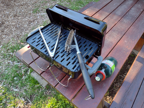 Compact propane grill, tools, and Coleman tank ready for RV rental outdoor cooking on a picnic table.