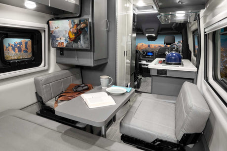 Experience an RV rental: a modern camper van interior featuring a comfortable dinette with TV and a full kitchenette.