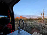 Experience RV rental life: a modern sink overlooks a stunning Arizona desert with saguaros and sunset-lit mountains.