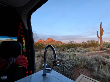 Experience RV rental life: a modern sink overlooks a stunning Arizona desert with saguaros and sunset-lit mountains.