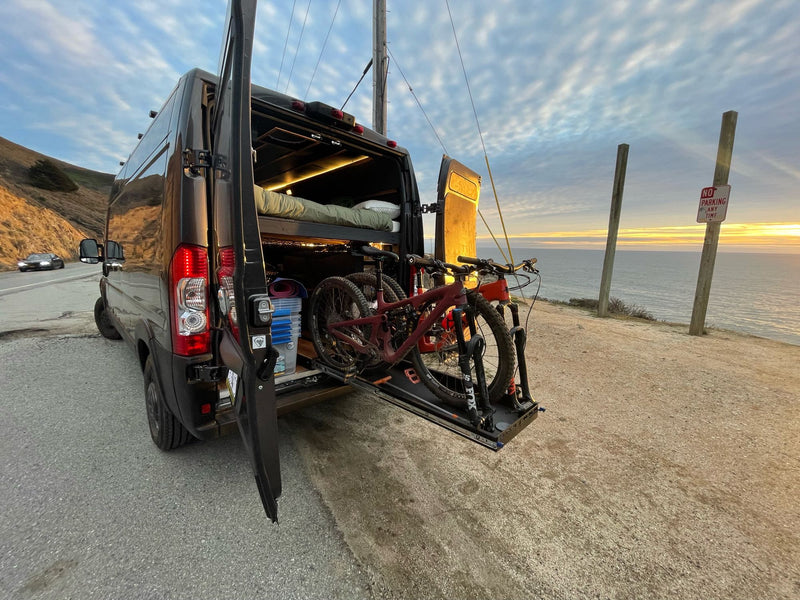  framed by spectacular red rock mountains. A digital nomad's workspace.|Workstation in a cozy RV rental: A laptop sits on a wooden desk with sleek cabinets and ambient lighting. A person is visible inside.|Dark gray Ram ProMaster van (potential RV rental) parked near striking red rock formations under a clear blue sky — photo 9