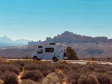 White RV rental parked on a scenic desert road, with distant red rock mountains layered against a clear blue sky. Perfect for a road trip.