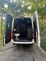 RV rental ready for travel! Rear view of a white camper van with open doors, revealing a compact toilet and sink area.