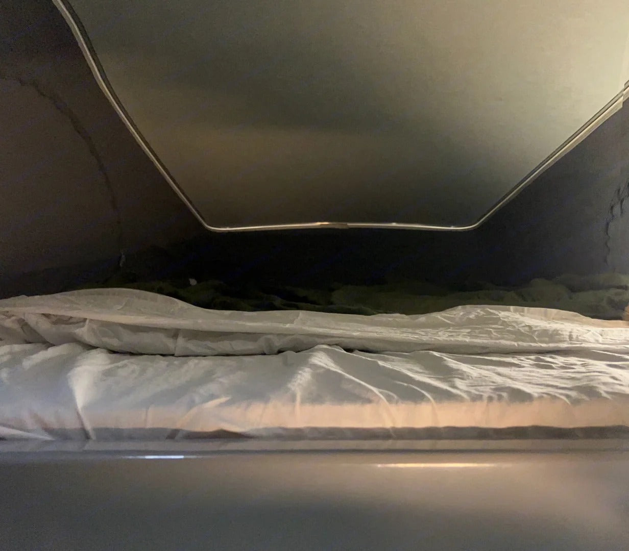 Low-angle view inside an RV rental: a cozy pop-top bed with white sheets and blankets.