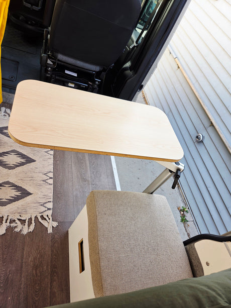 RV rental workspace: Light wood table, upholstered bench seat, patterned rug, and wood-look floor. An open door reveals a house exterior.