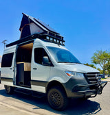Mercedes-Benz Sprinter RV rental: A custom camper van with a pop-top, off-road tires, & lights, parked under a blue sky.