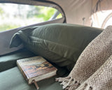 Inside an RV rental: a comfy bed with a green pillow, knitted blanket, and 'Wanderlust' book, hinting at adventure.