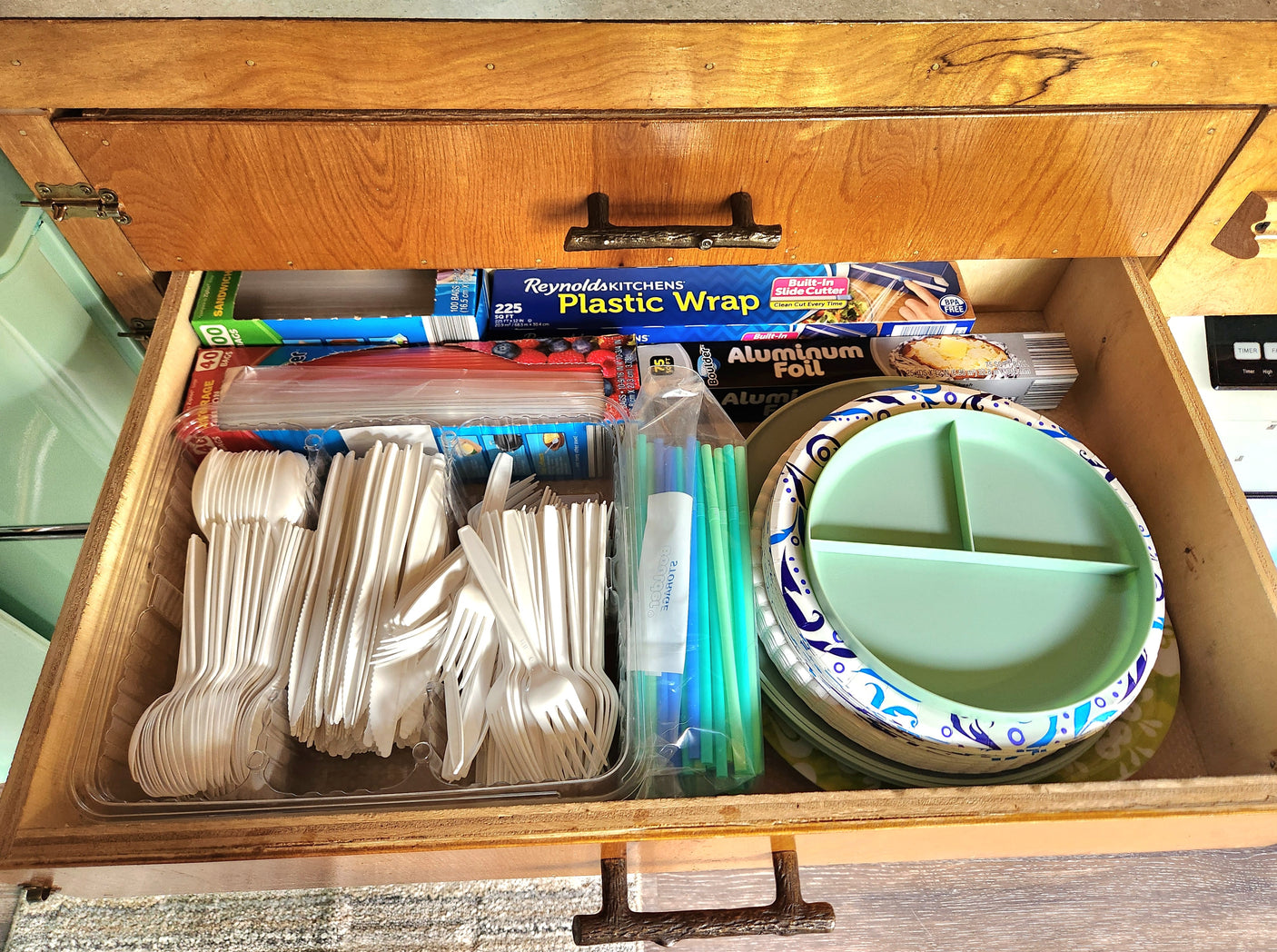 Essential kitchen supplies neatly stored in an RV rental drawer: plastic wrap, foil, bags, cutlery, and plates.