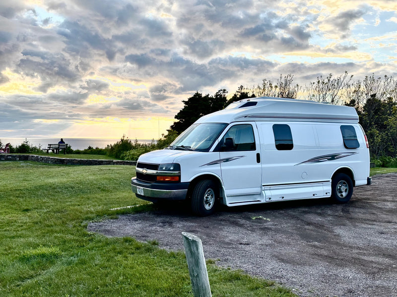 A white RV rental van with a raised roof is parked on gravel, overlooking a stunning ocean sunset and cloudy sky. — photo 3