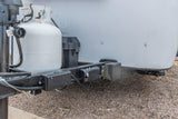 Close-up of an RV rental's front, showing propane tank, battery box, and vital electrical connections on the trailer hitch.