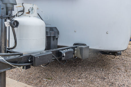 Close-up of an RV rental's front, showing propane tank, battery box, and vital electrical connections on the trailer hitch.
