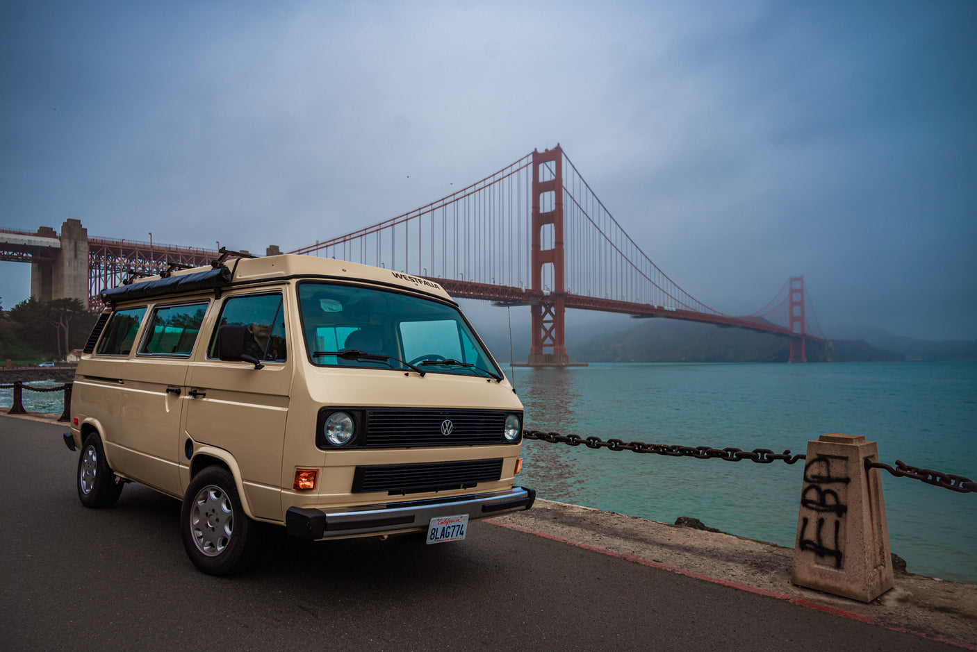 Explore San Francisco with an RV rental! A beige VW Westfalia parked by the Golden Gate Bridge, showcasing coastal travel.