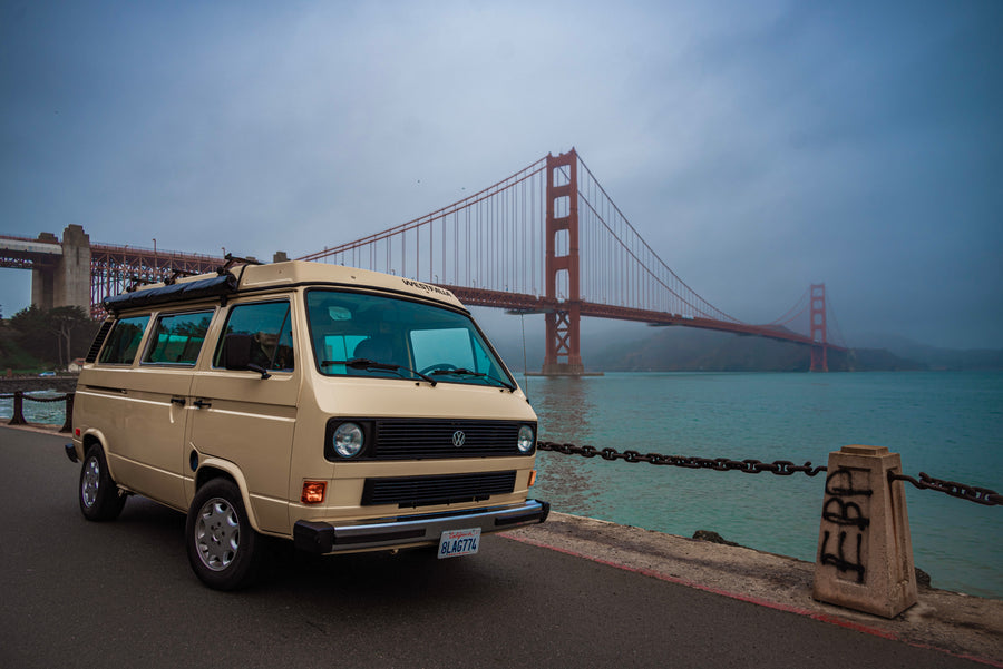Explore San Francisco with an RV rental! A beige VW Westfalia parked by the Golden Gate Bridge, showcasing coastal travel.