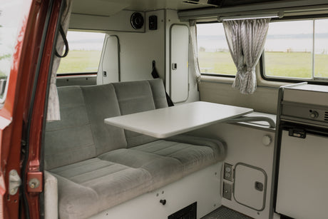 Cozy RV rental interior with grey seating, extendable table, and scenic window views of a green landscape.