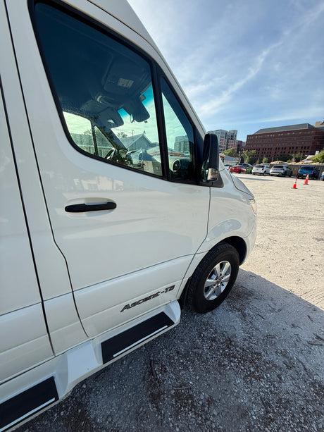 White Mercedes Sprinter RV rental. Side view of this Ascent-TS motorhome conversion parked on a gravel lot under a blue sky.