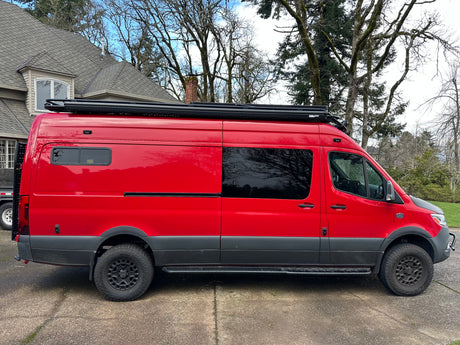Custom bright red adventure van, ideal for rv rental. Features off-road tires, a roof rack, and a unique look.