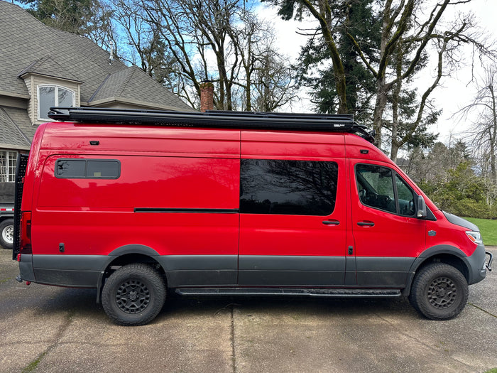 Custom bright red adventure van, ideal for rv rental. Features off-road tires, a roof rack, and a unique look.