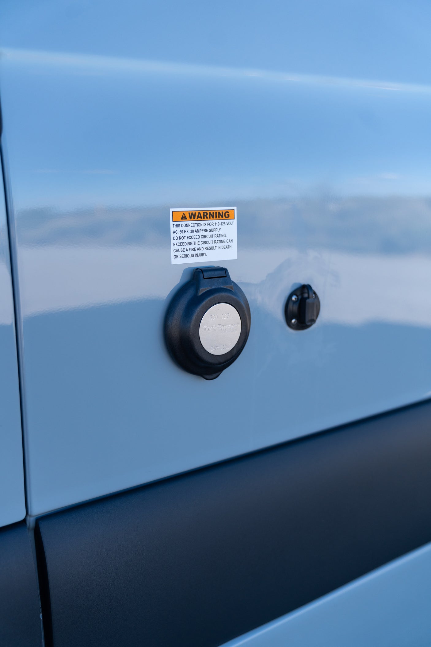 RV rental's 30A 125V electrical power inlet with a clear warning label, essential for safe and proper RV hookup.