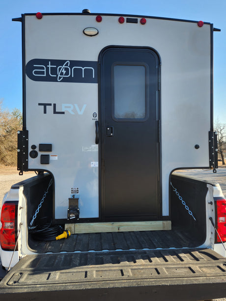Back of an Atom TLRV truck camper in a pickup, ready for RV rental adventures. Shows door & utility hookups.
